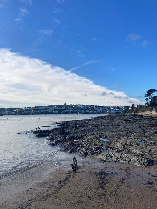 Sandy beach with rocky foreshore behind it, Falmouth town in the distance over the river.